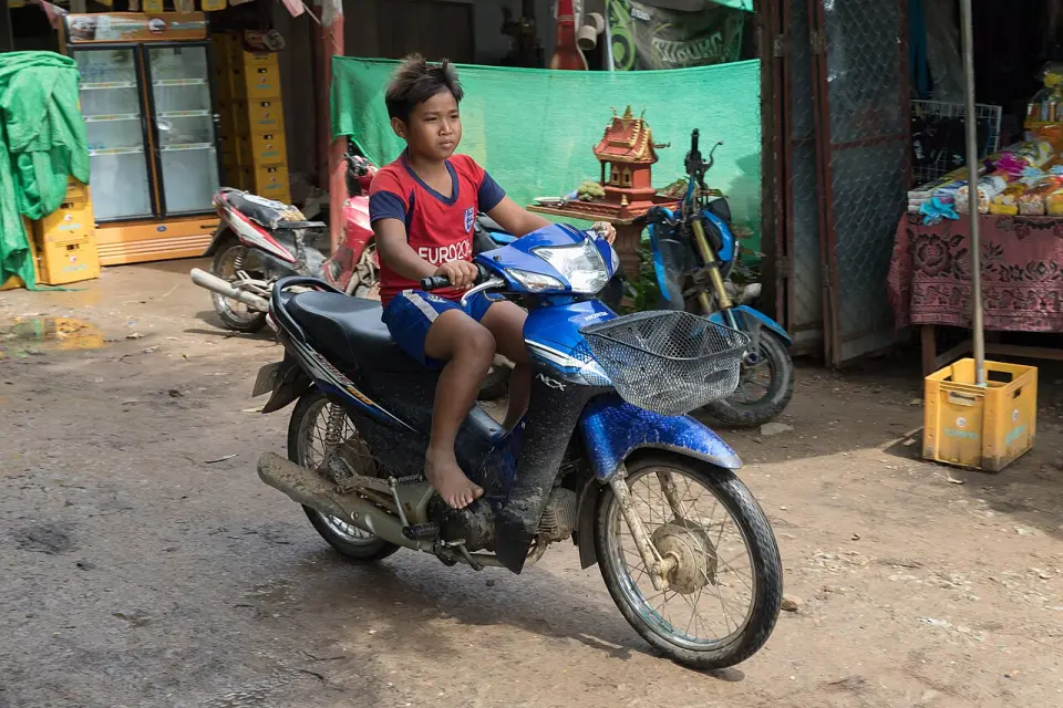 A young rider on a motorbike on a village road in Laos
